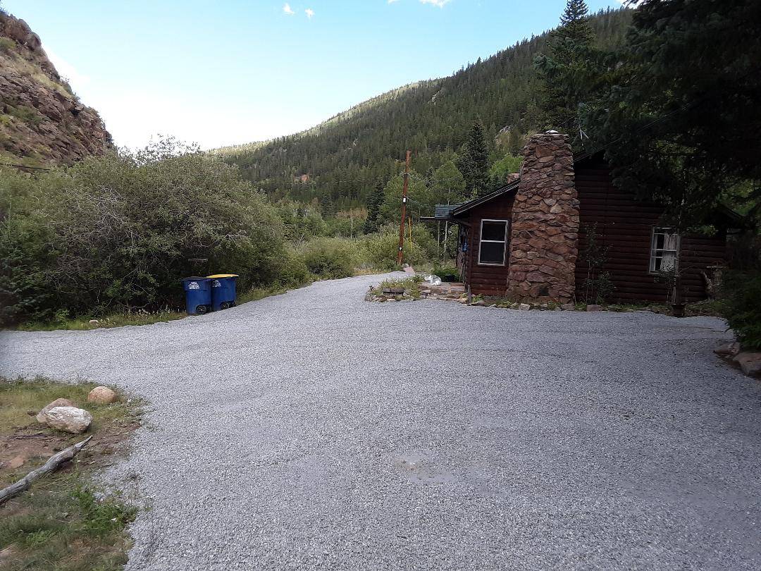 Finished gravel driveway in front of a log cabin with a stone chimney in a mountain canyon
