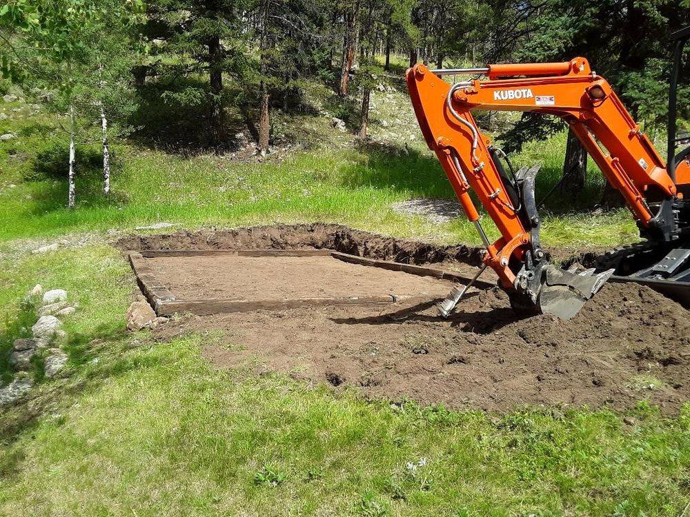 Kubota excavator beside a leveled dirt pad framed with timber