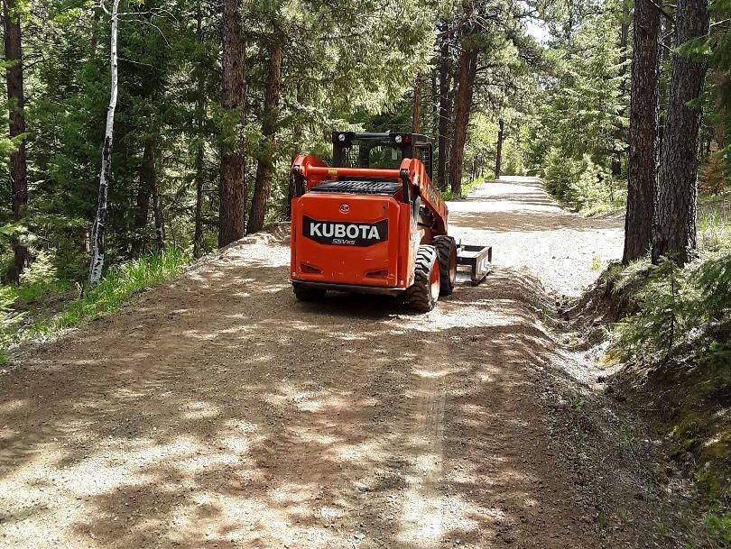 Kubota skid steer grading a wooded mountain road